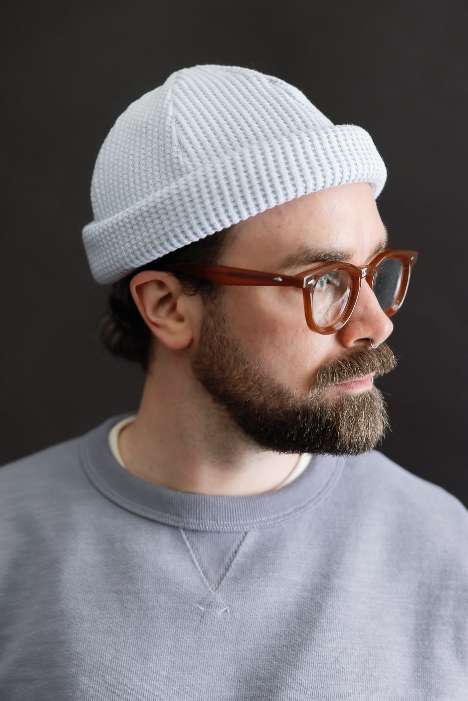JM6607 - Waffle Knit Cap - 425 Ice Blue is showcased on a bearded man in profile, paired with tortoiseshell glasses and a gray sweatshirt, illustrating its versatile, longer design.