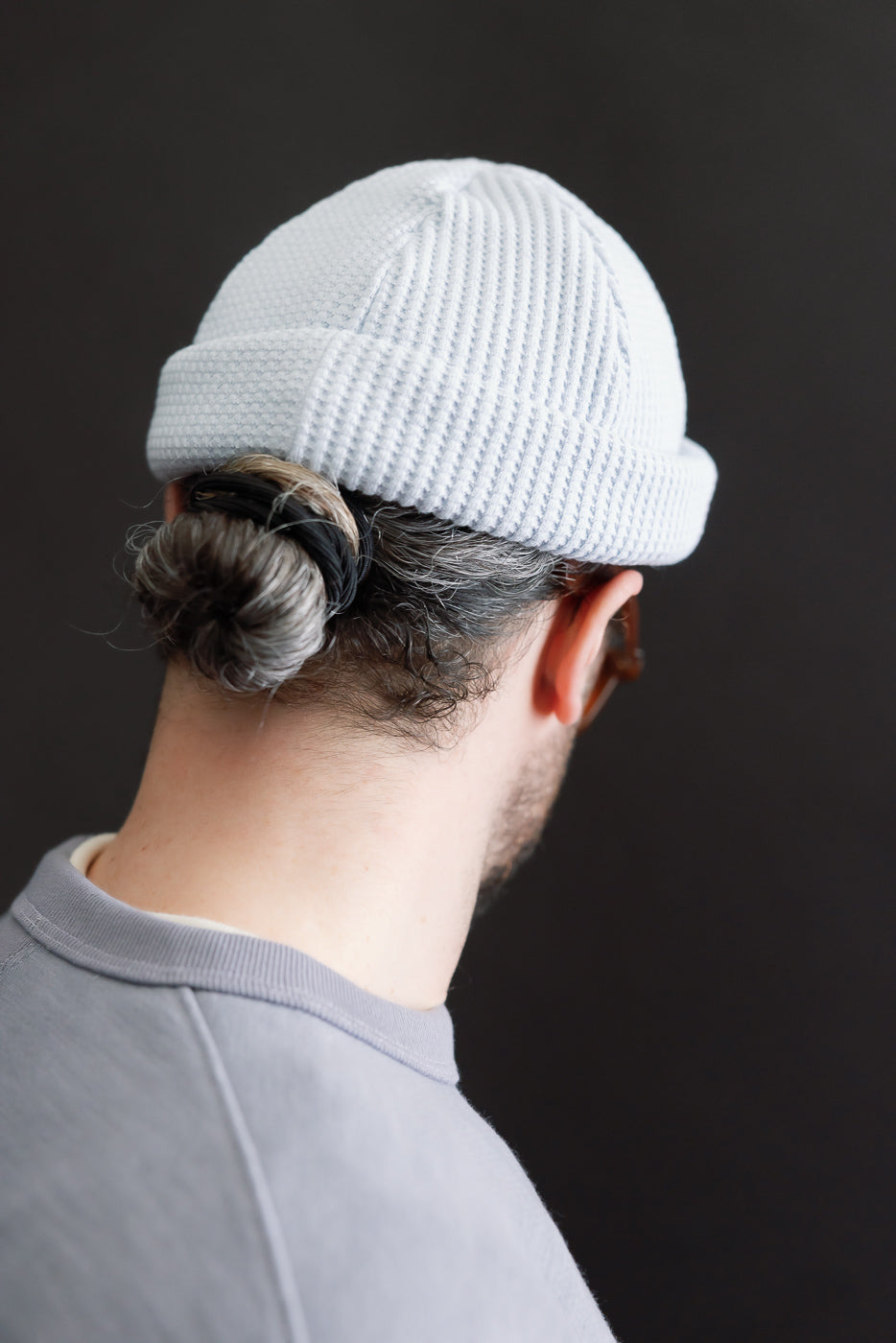 Person wearing JM6607 - Waffle Knit Cap in a light color, showcasing its textured waffle-knit design and rolled-up brim, with hair pulled into a bun, highlighting the cap's versatile fit.