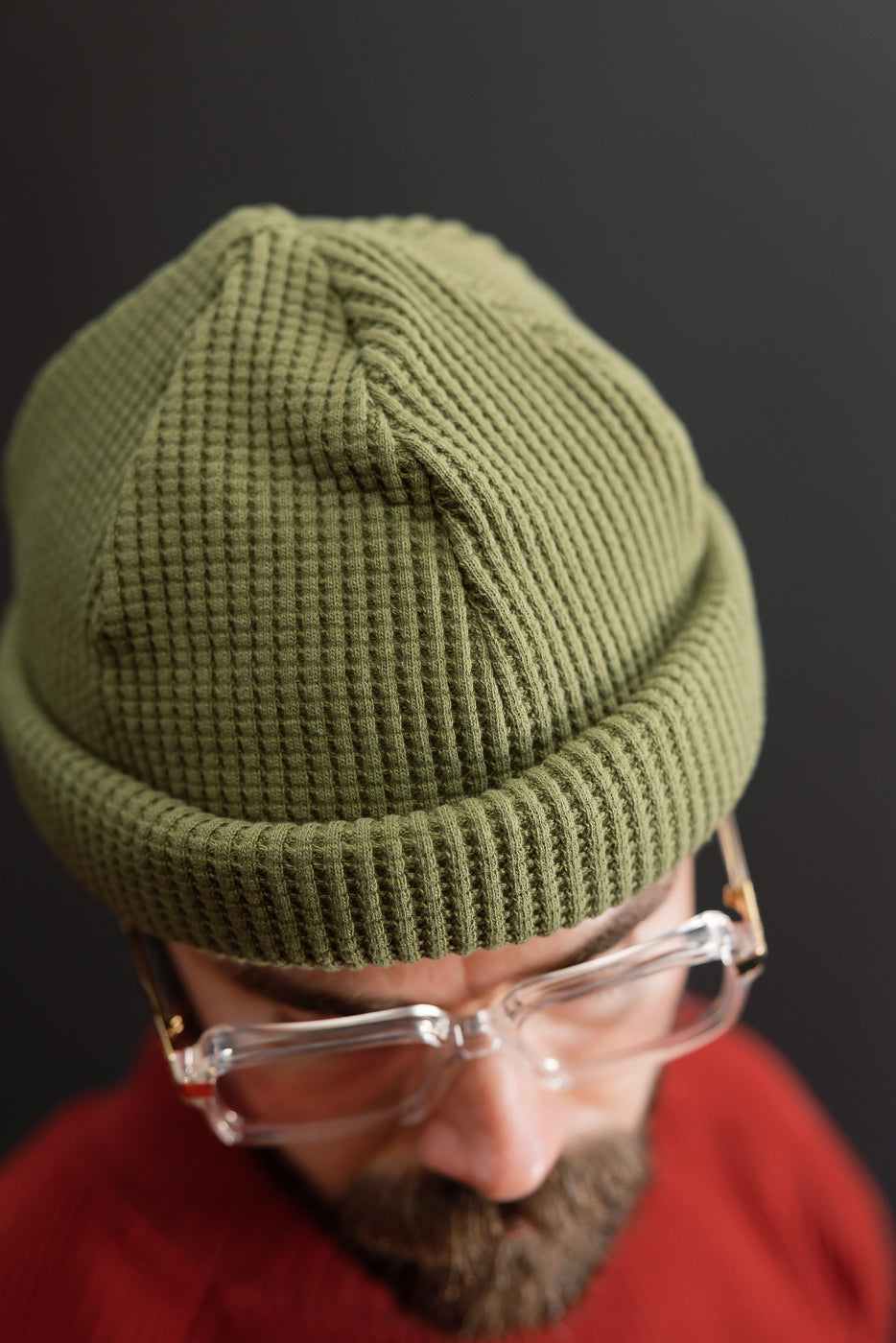 Close-up front view of an olive green waffle-knit beanie on a male model.