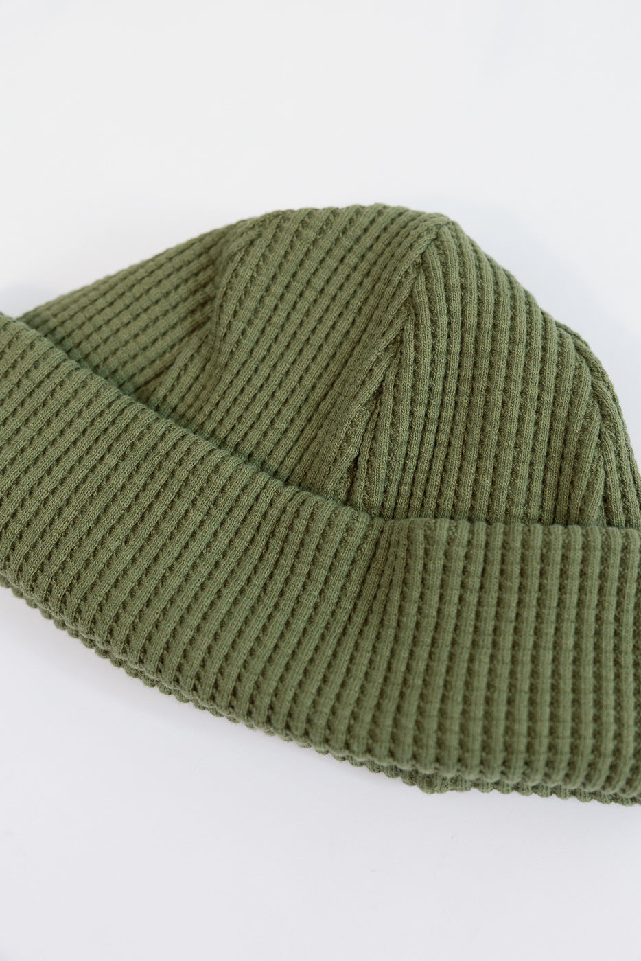 Close-up of the front and side of an olive green ribbed knit beanie.