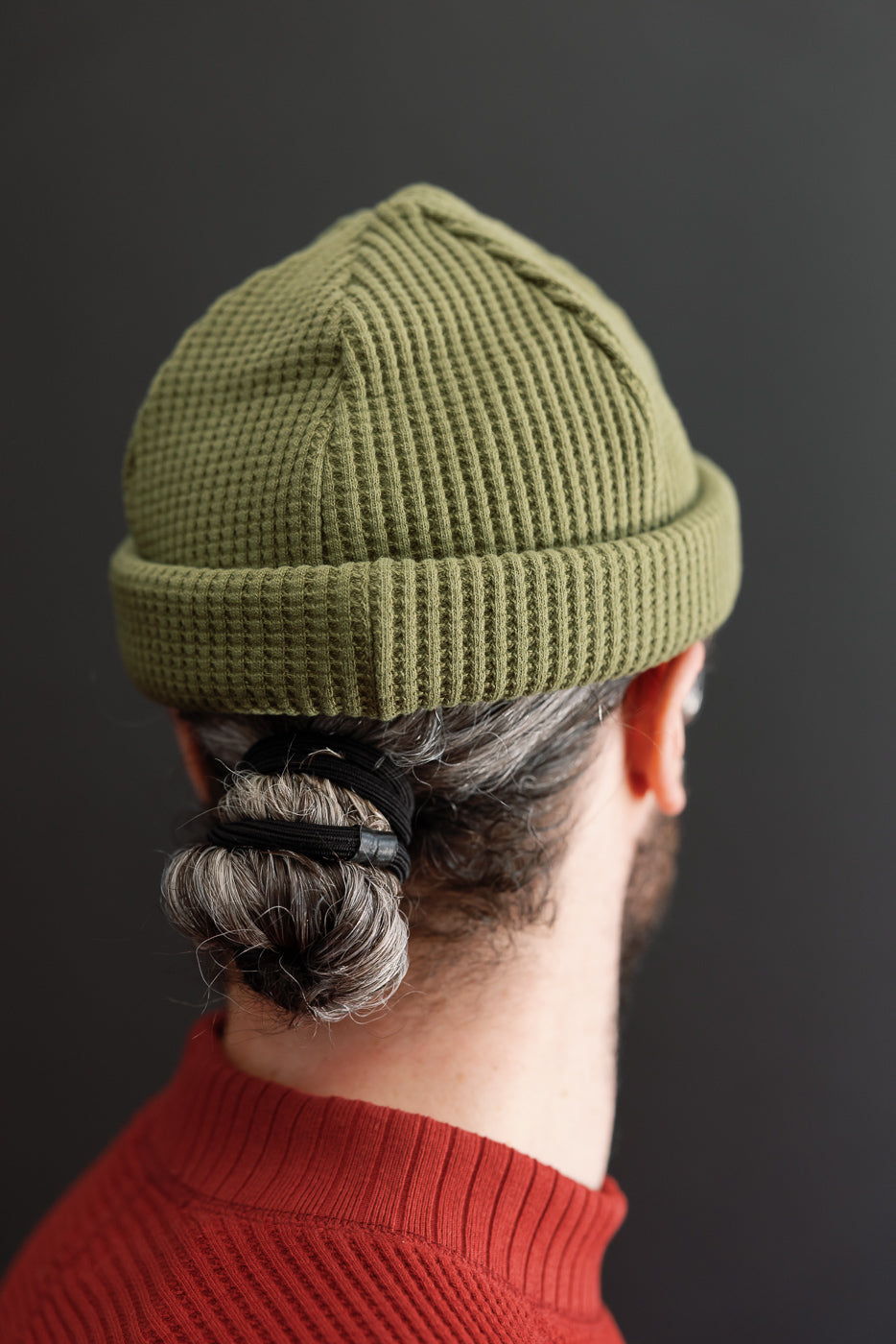 Back view close-up of an olive green waffle knit beanie on a male model.
