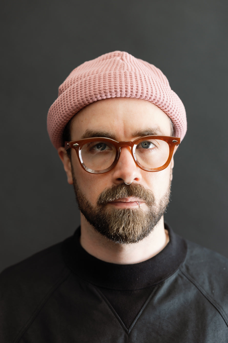 JM6607 - Waffle Knit Cap - 448 Old Raspberry showcased on a bearded man with tortoiseshell glasses and a septum ring, highlighting the cap's unique texture and versatile fit.