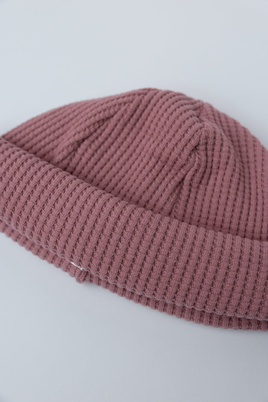JM6607 - Waffle Knit Cap - 448 Old Raspberry, a folded dusty-rose waffle-knit beanie, showcasing its unique texture and versatile length, laid flat on a light surface.