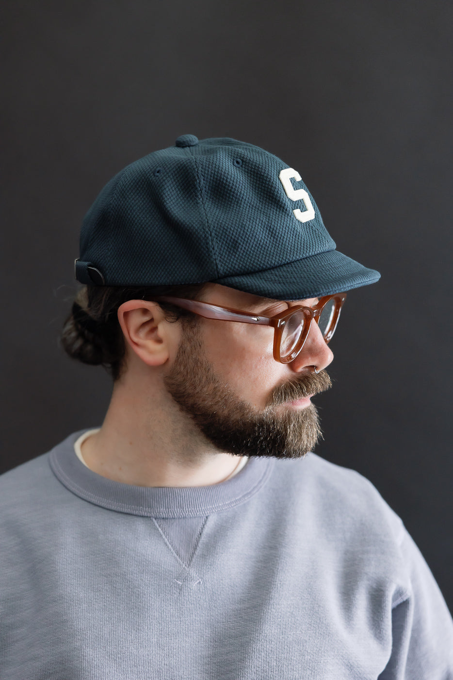 JM6623 - Sashiko BB Cap S - 280 Iron Navy worn by a bearded man, showcases a dark, textured baseball cap with a raised S on the front, embodying sashiko fabric's historical craftsmanship.