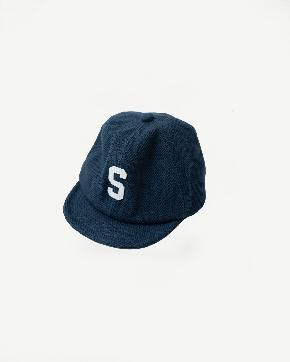 JM6623 - Sashiko BB Cap S - 280 Iron Navy features a textured, navy-blue sashiko fabric with a white S on the front, showcasing detailed craftsmanship and historical fabric significance.