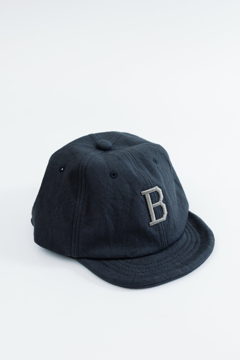 Front view close-up of a navy blue baseball cap with a grey embroidered letter B.