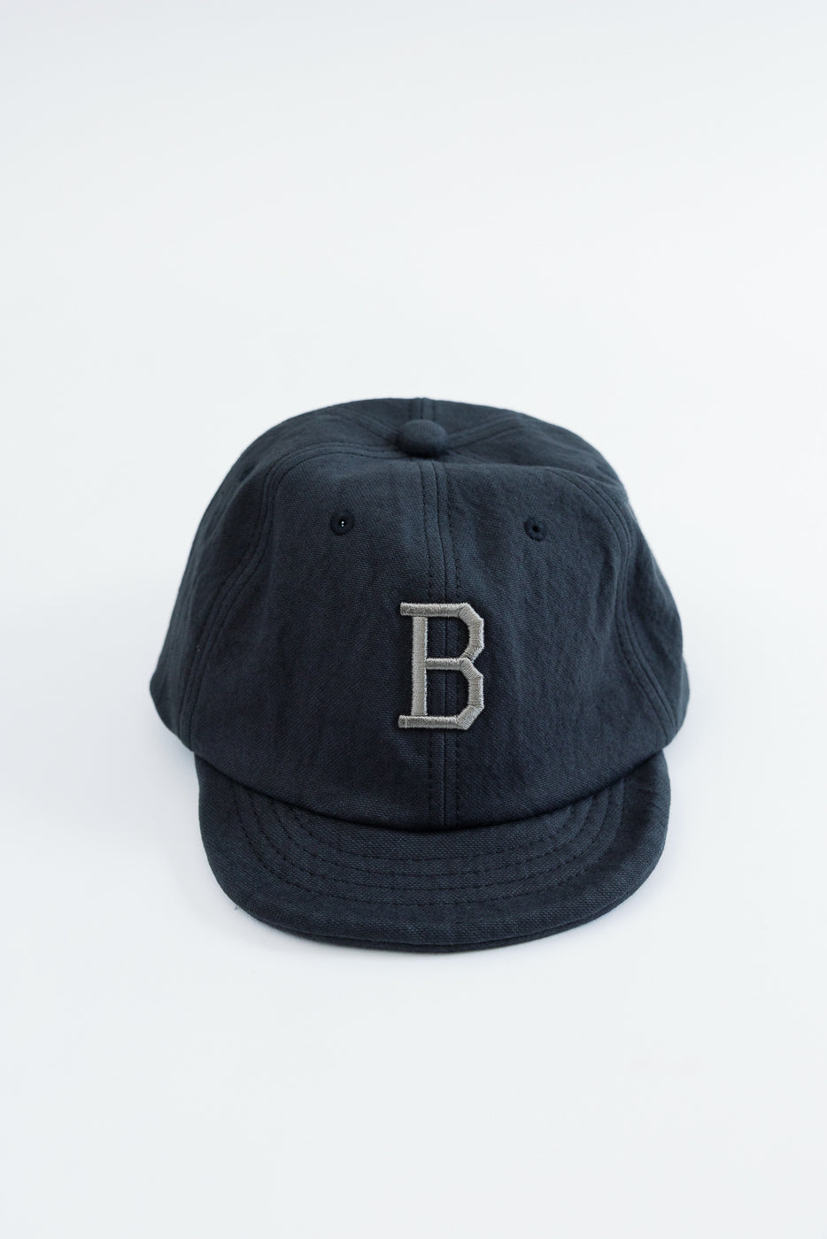 Front view of a navy blue cotton baseball cap with a grey embroidered letter B.