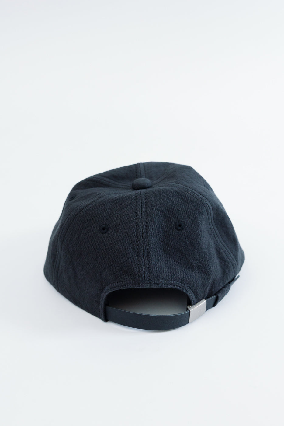Back view close-up of a black cotton baseball cap with an adjustable strap and silver buckle.