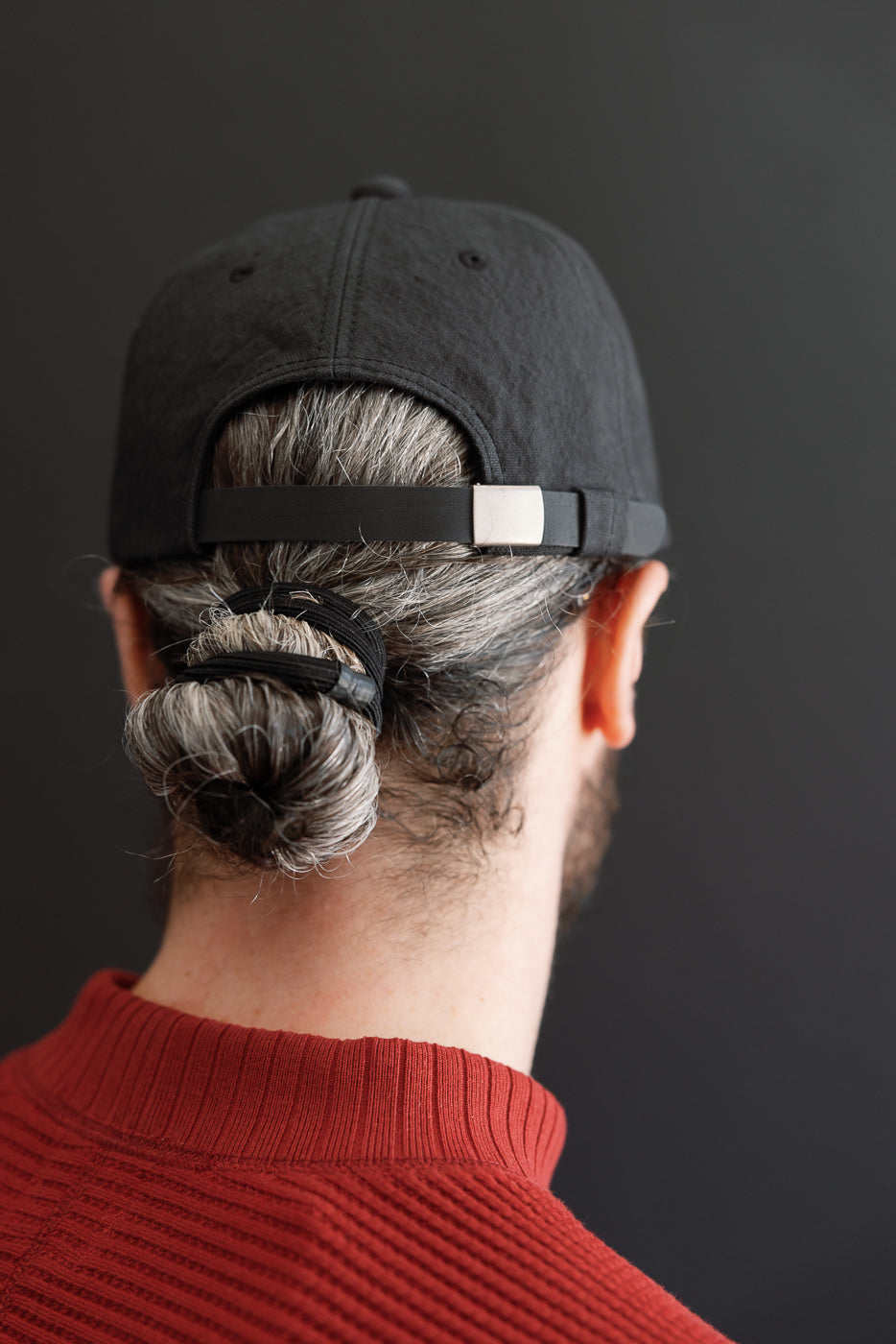 Close-up back view of a male model wearing a black cotton baseball cap and red ribbed sweater.
