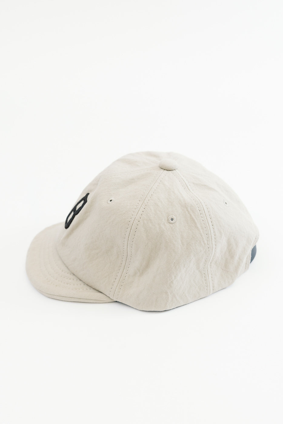 Side view close-up of a beige cotton baseball cap showing fabric texture and eyelets.