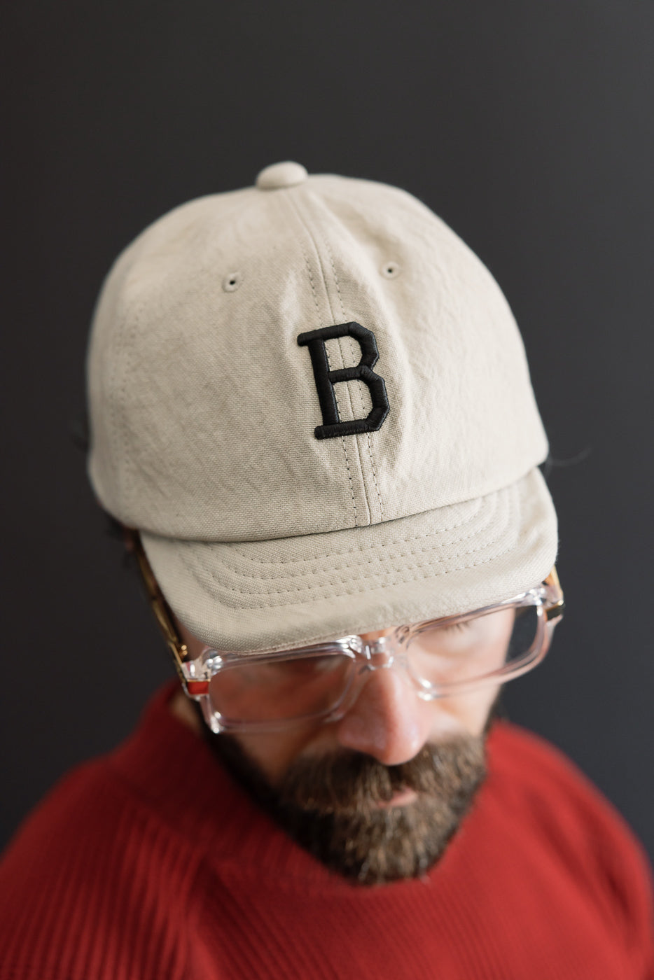 Close-up front view of a male model wearing a beige canvas baseball cap with a black letter B.