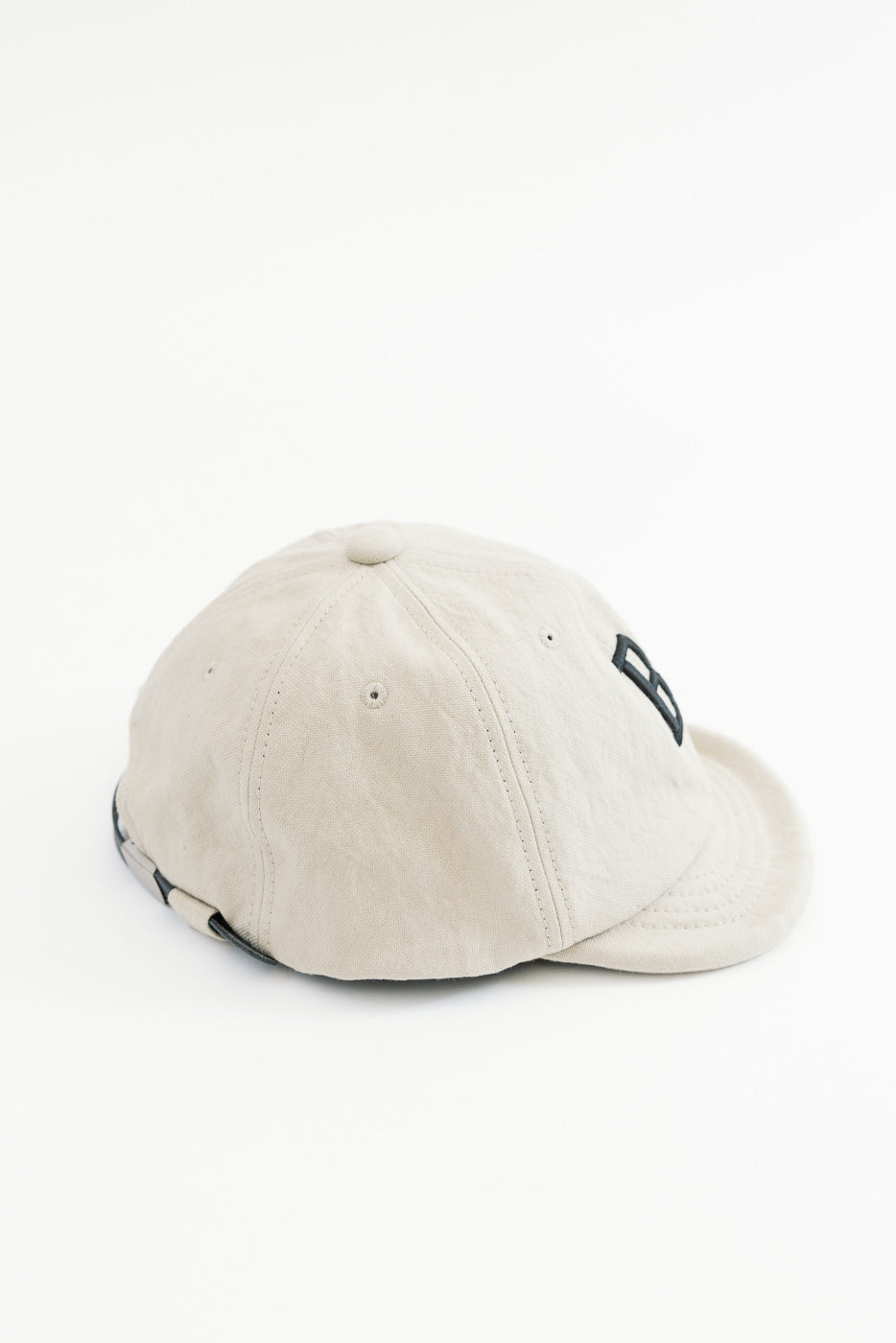 Side view close-up of a beige cotton baseball cap showing the side panel and brim.