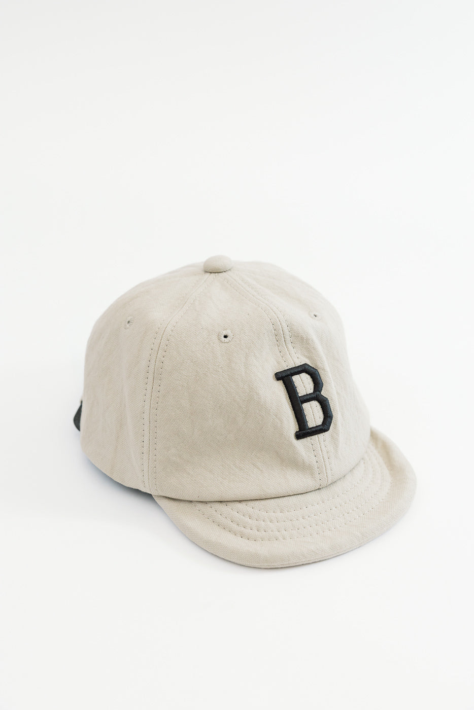 Front view of a beige baseball cap featuring a black embroidered letter B.