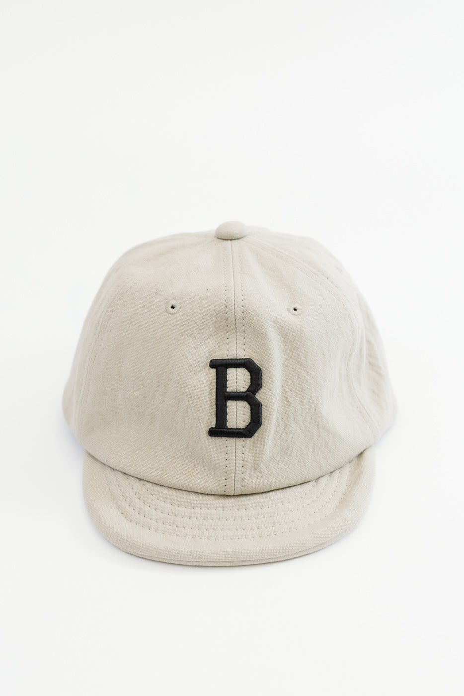 Front view of a beige cotton baseball cap featuring a black embroidered letter B.