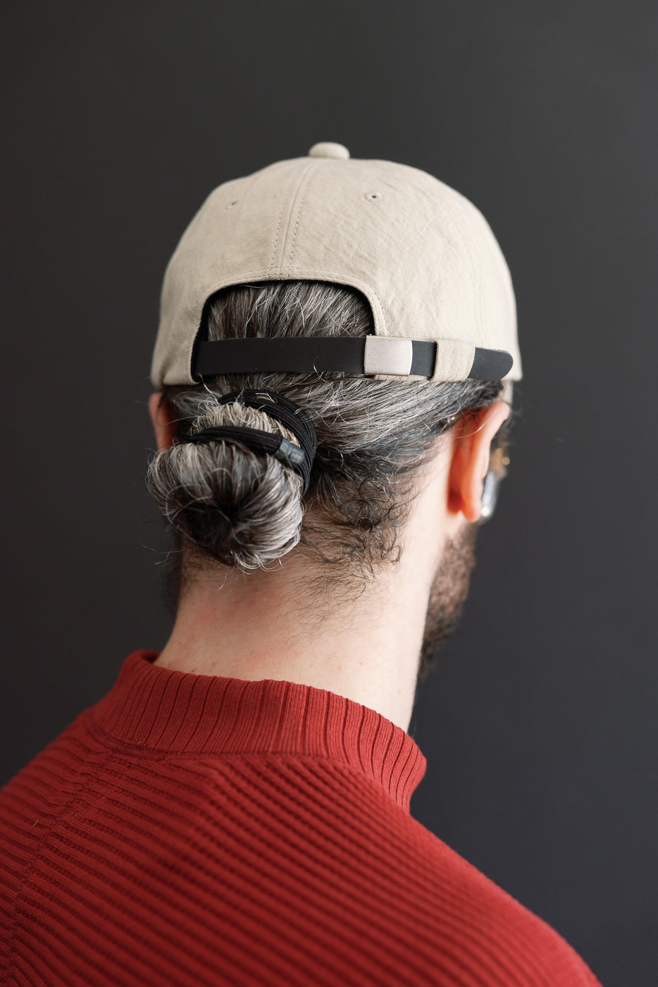 Close-up back view of a male model wearing a tan baseball cap and red ribbed sweater.