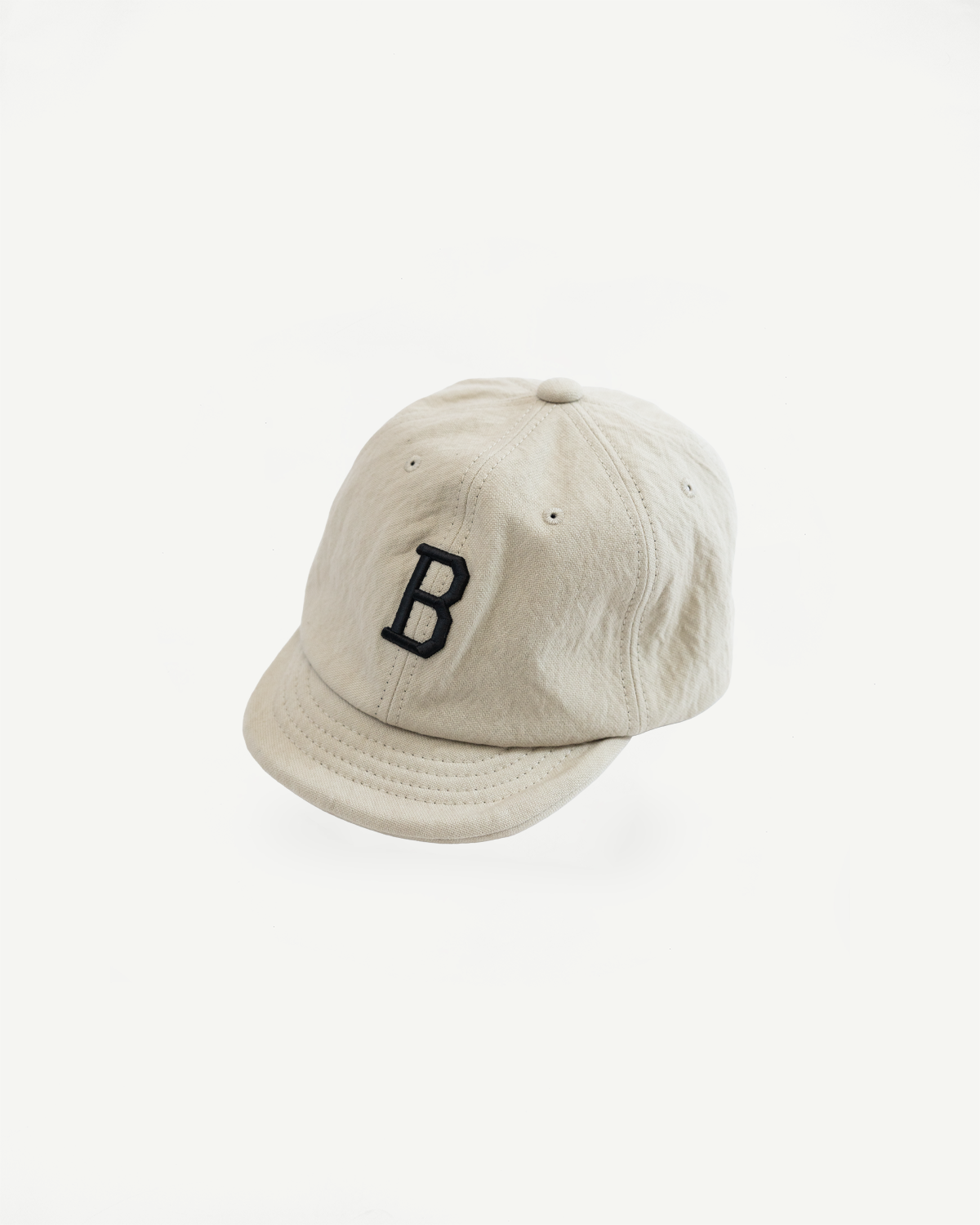 Front view close-up of a cream cotton baseball cap with a black embroidered letter B.