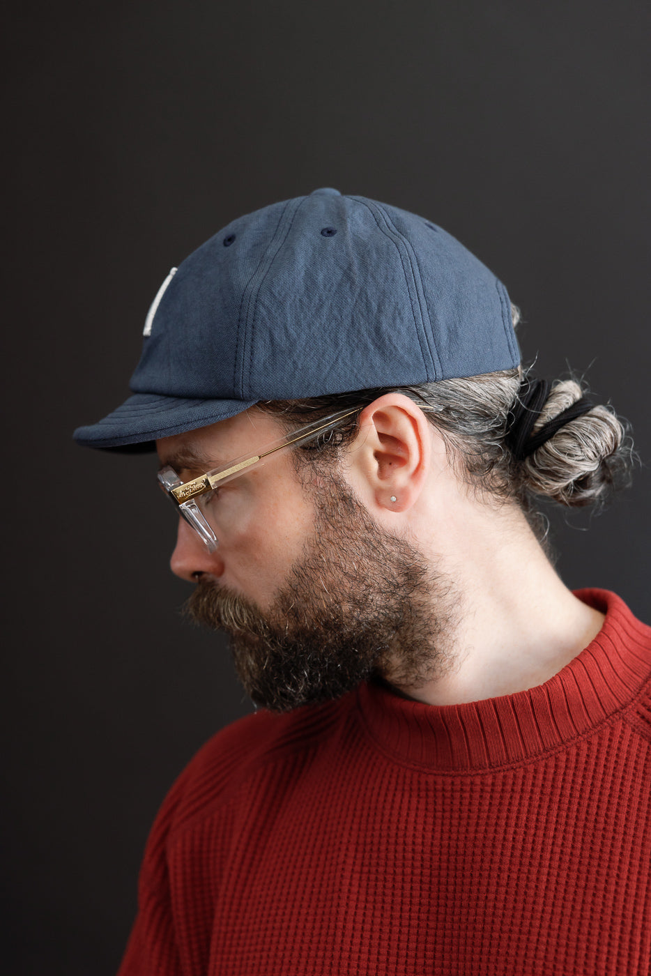 Side profile close-up of a male model wearing a navy blue baseball cap and red waffle knit sweater.