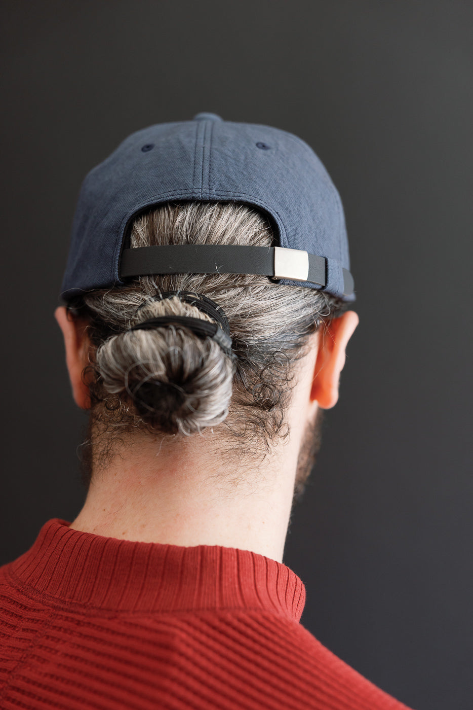 Back view close-up of a male model wearing a navy blue baseball cap with a black adjustable strap.