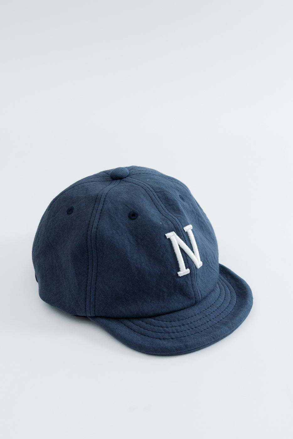 Front view close-up of a navy blue cotton baseball cap featuring a white embroidered letter N.