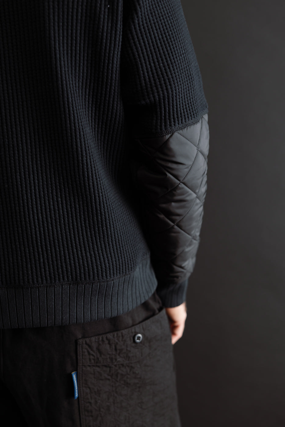 Close-up side view of a black ribbed knit sweater with quilted diamond-patterned sleeves.