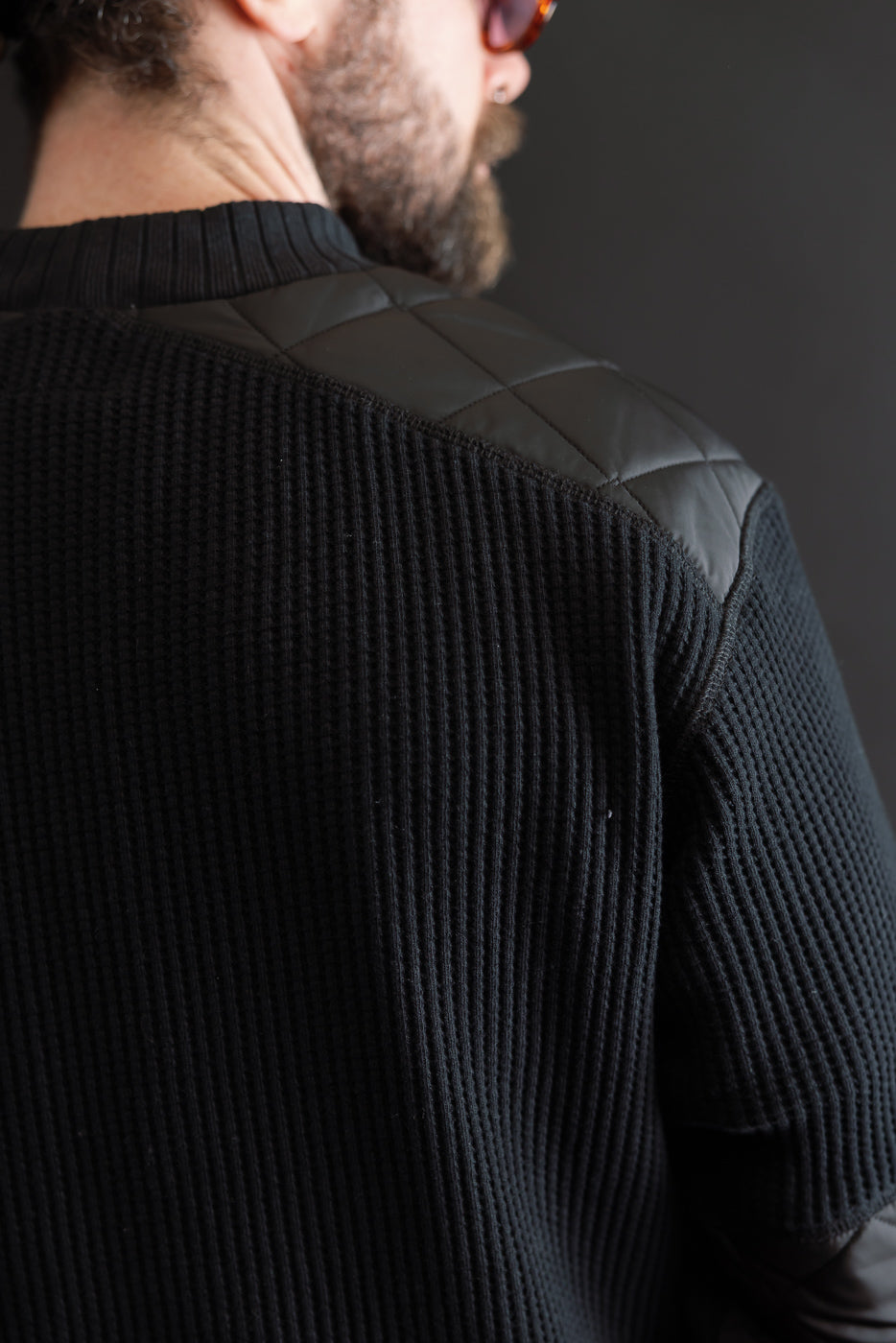 Close-up back view of a black ribbed sweater with quilted leather shoulder patches on a male model, 5'9