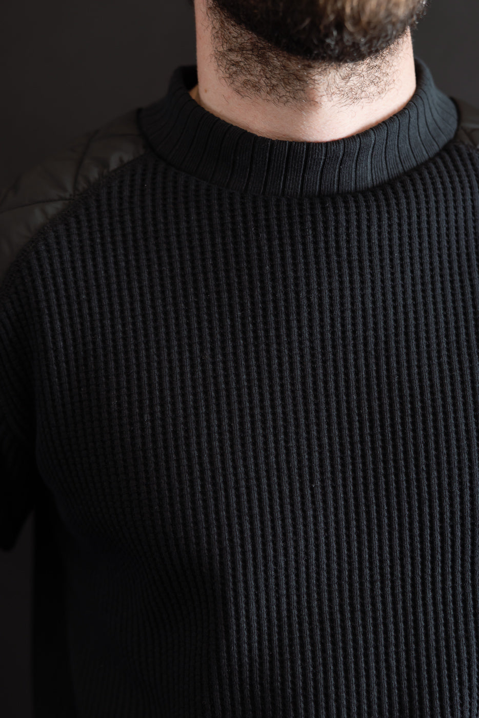 Close-up front view of a black ribbed knit sweater texture and crew neck collar on a male model.