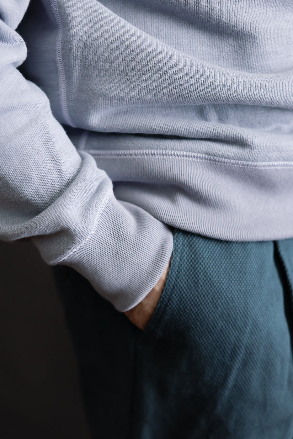 Close-up of midsection wearing JM7292 - GG Sweat Crewneck, showcasing its grainy-textured fabric and reinforced seams, with hand in pocket of dark, textured pants, highlighting Dant's premium menswear aesthetic.