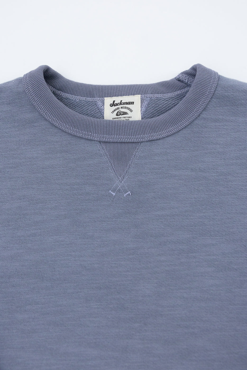 JM7292 - GG Sweat Crewneck: Displays a muted blue-gray crewneck with ribbed collar, V-stitch detail, and Jackman label. The grainy texture from twisted yarns emphasizes its unique, textural design.