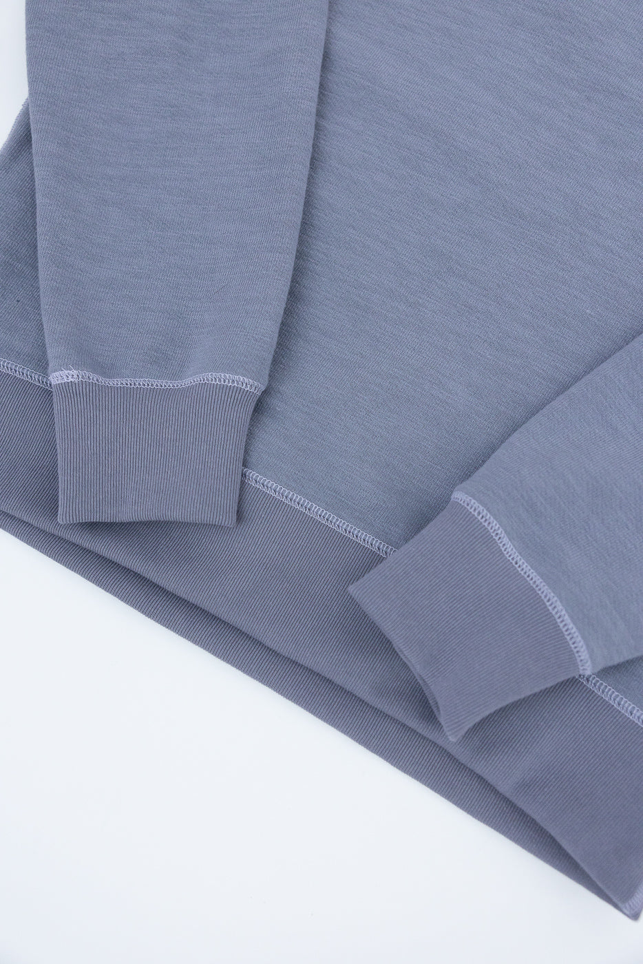JM7292 - GG Sweat Crewneck features a muted blue-gray color, ribbed cuffs, and hem, with visible overlock stitching. The sweatshirt's coarse texture and flatseam stitching highlight Jackman's craftsmanship.