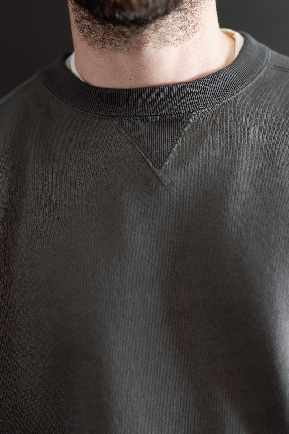 Close-up of the front neckline and collar of a dark grey crewneck sweatshirt on a male model.
