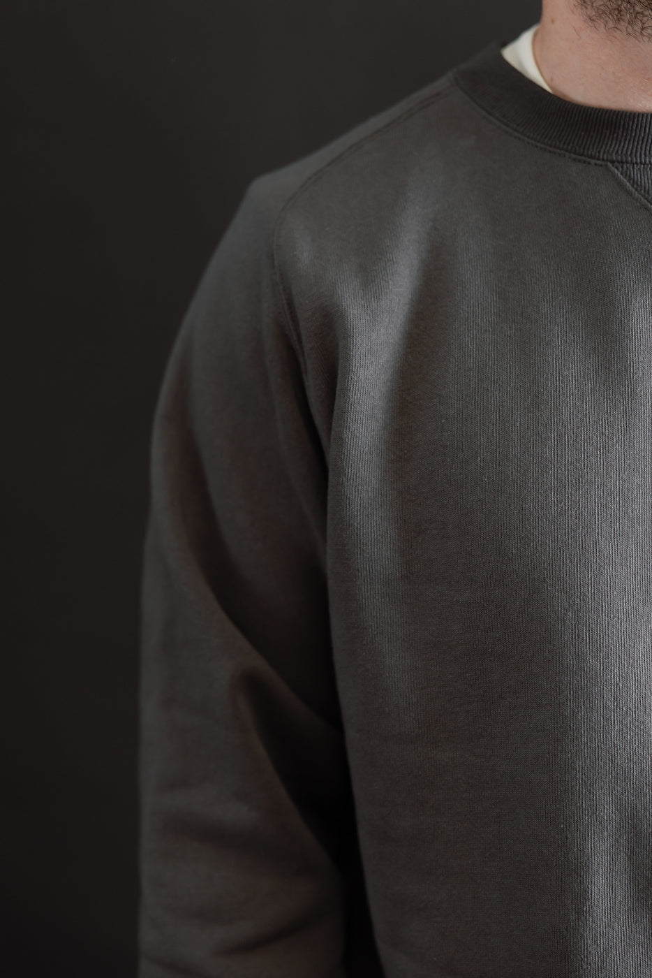 Close-up of the front and left side of a charcoal grey crewneck sweatshirt fabric texture.