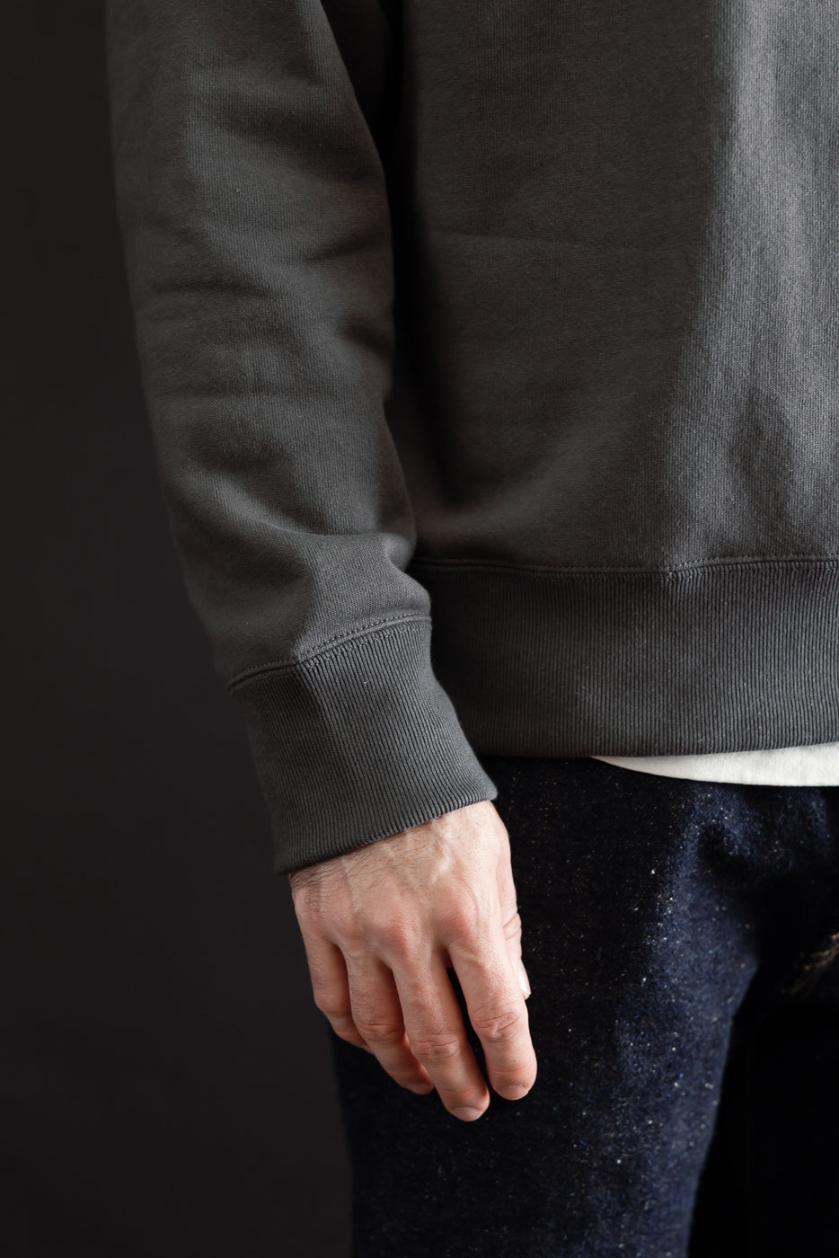 Close-up of the front side and ribbed cuff of a charcoal grey sweatshirt on a male model.