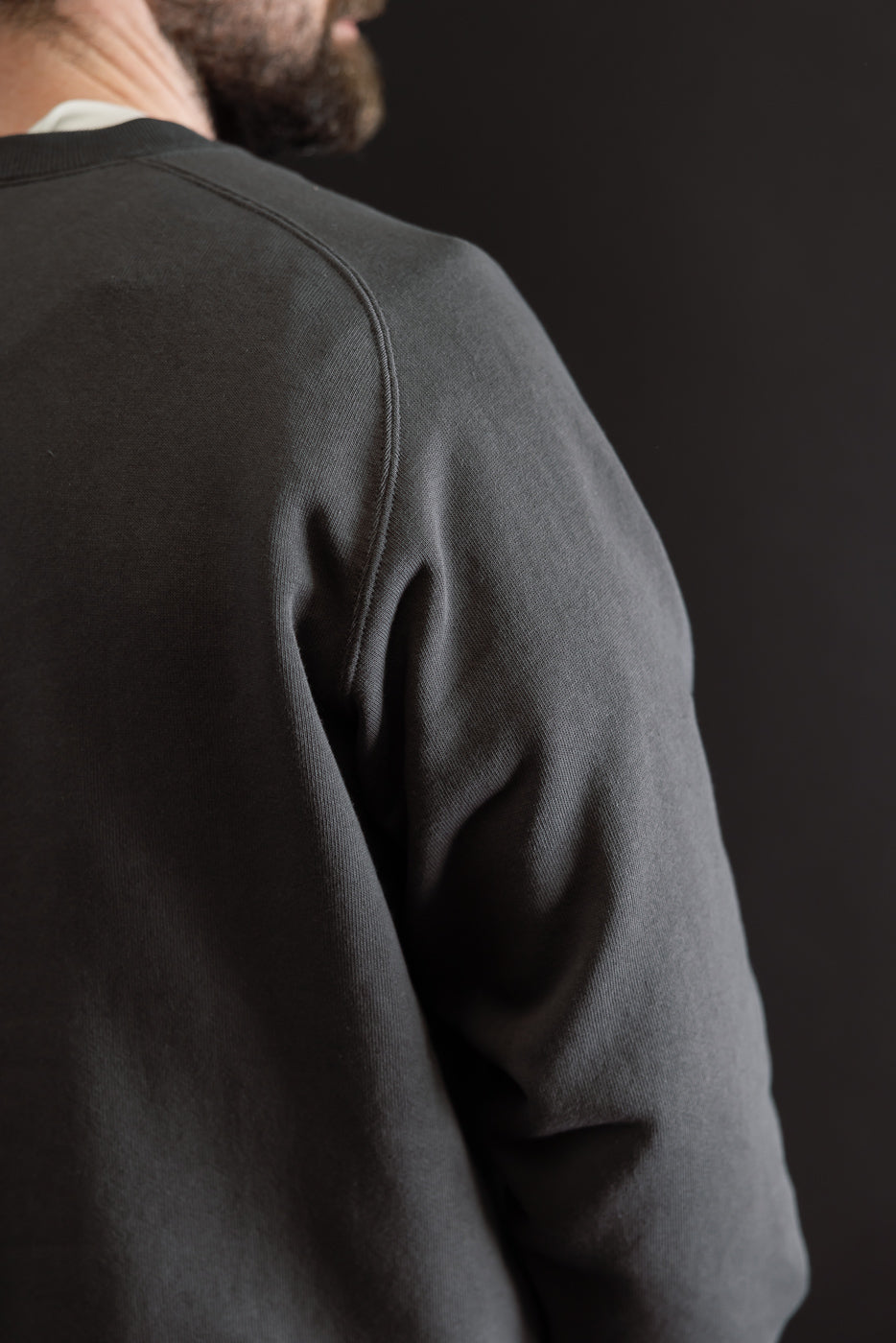 Close-up of the back and right sleeve of a charcoal grey sweatshirt on a male model.
