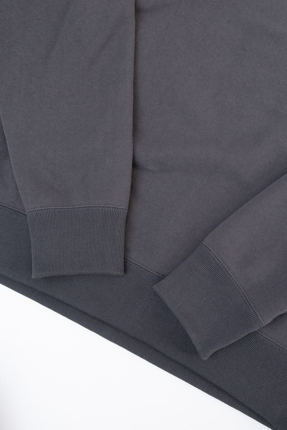 Close-up of the bottom hem and ribbed cuffs on a charcoal grey sweatshirt flat lay.