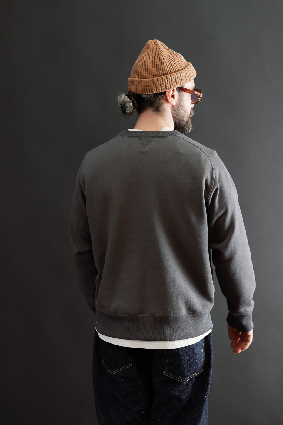 Back view of a charcoal grey sweatshirt on a male model, 5'9