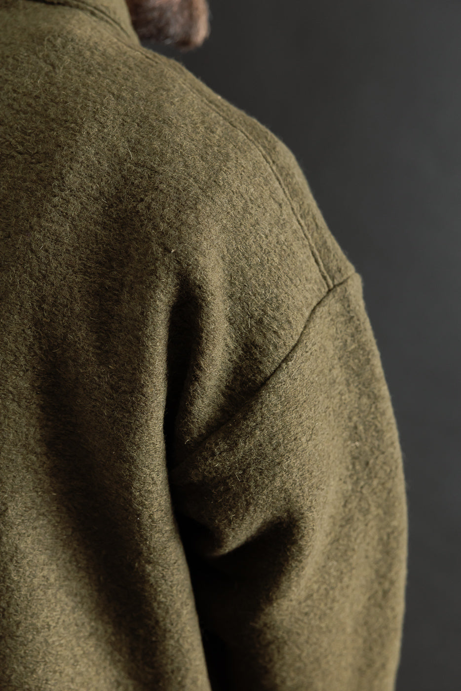 Close-up of male model’s back right shoulder in olive wool polo, showing fabric texture and seam detail.