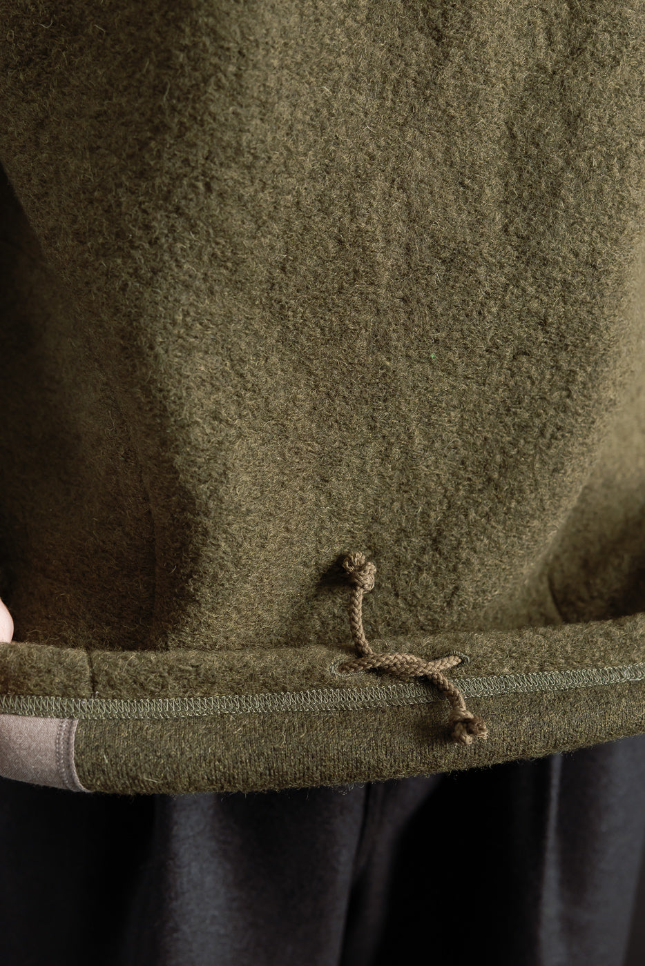 Close-up of olive wool polo hem front with drawstring detail and textured fabric.