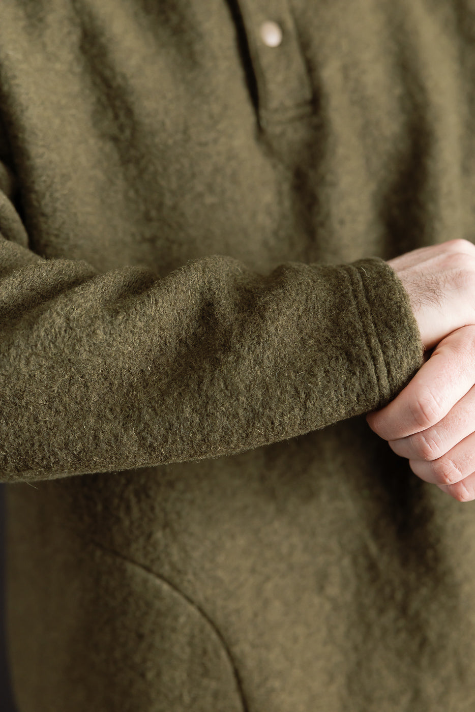 Close-up of male model’s arm in olive wool polo, highlighting sleeve texture and cuff detail.