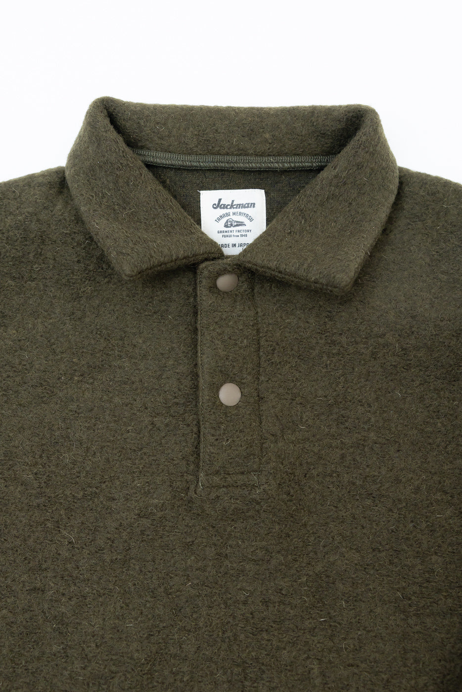 Close-up front view of olive wool polo shirt, highlighting textured fabric, collar, buttons, and tag.