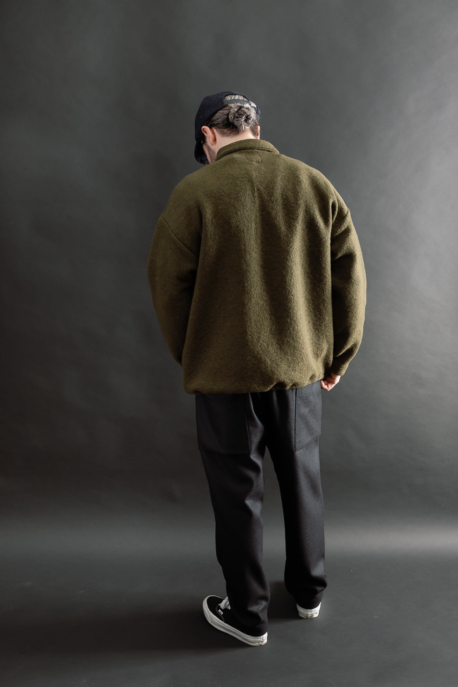 Full body back view of male model 5'9, 165lbs athletic build wearing olive wool polo long sleeve shirt and black pants