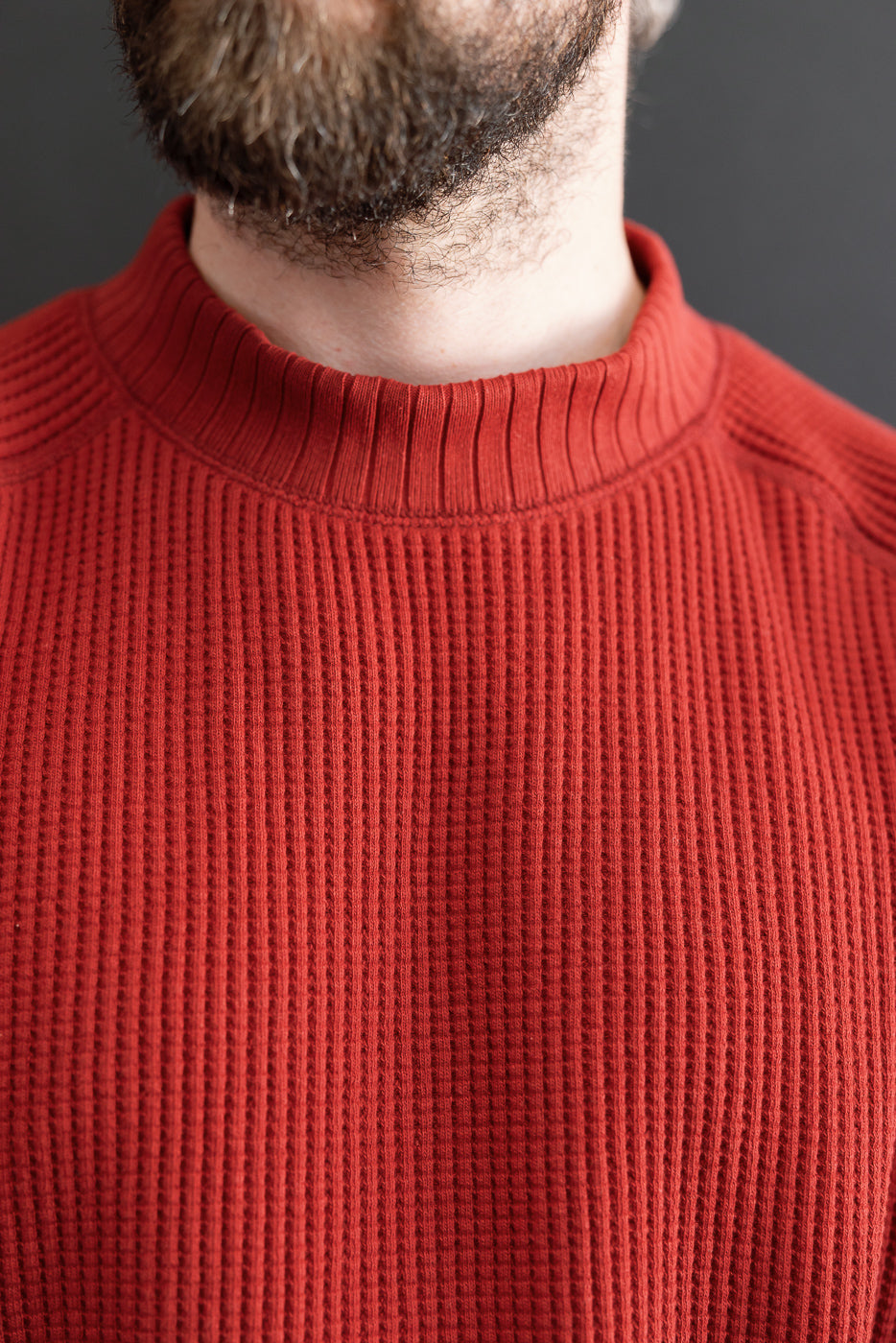 Close-up front view of a red waffle-knit sweater collar on a male model.