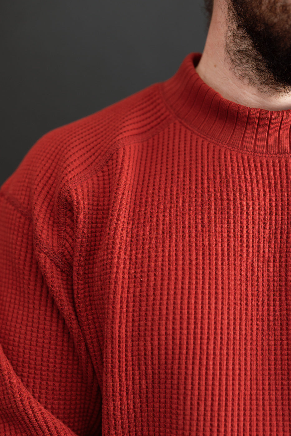 Close-up of the front neckline and shoulder of a red waffle-knit sweater on a male model.
