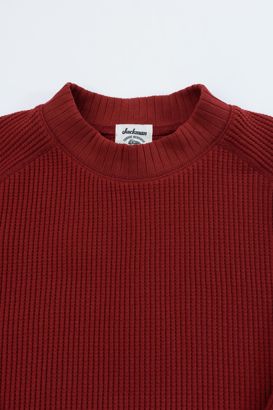 Close-up of front neckline, waffle texture and tag on a red Jackman sweater.