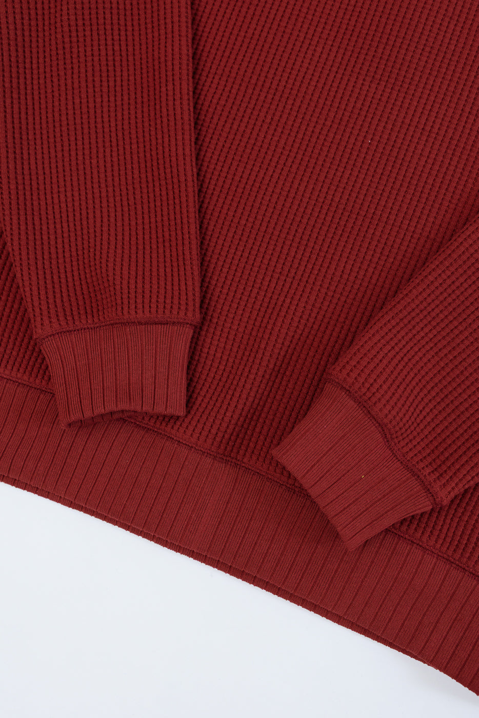 Close-up flat lay of a red waffle-knit sweater showing ribbed cuffs and hem.