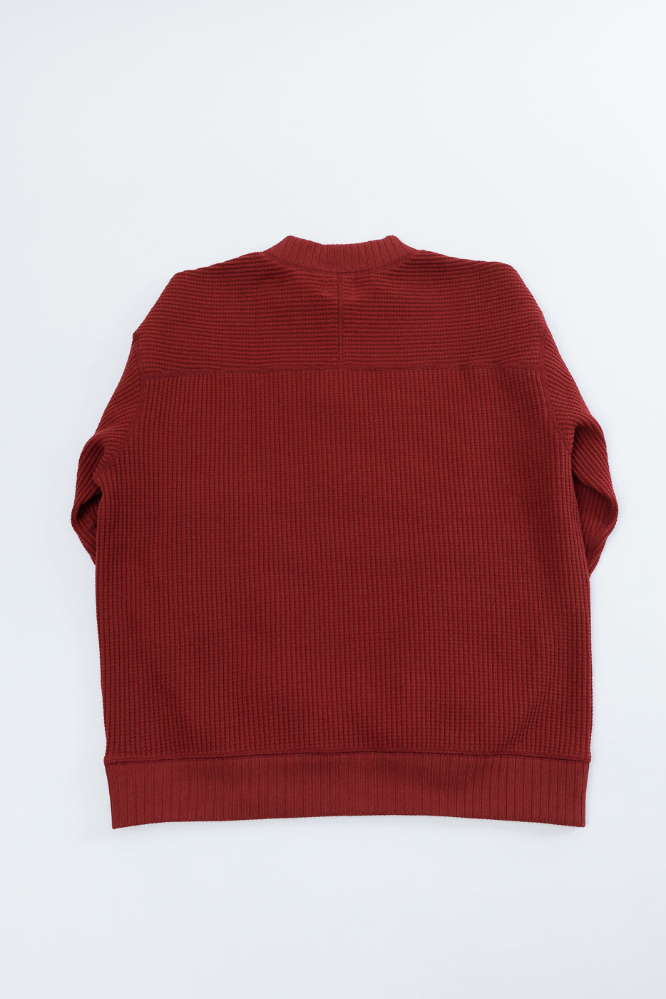 Flat lay of the back of a red waffle knit sweater with a ribbed hem.