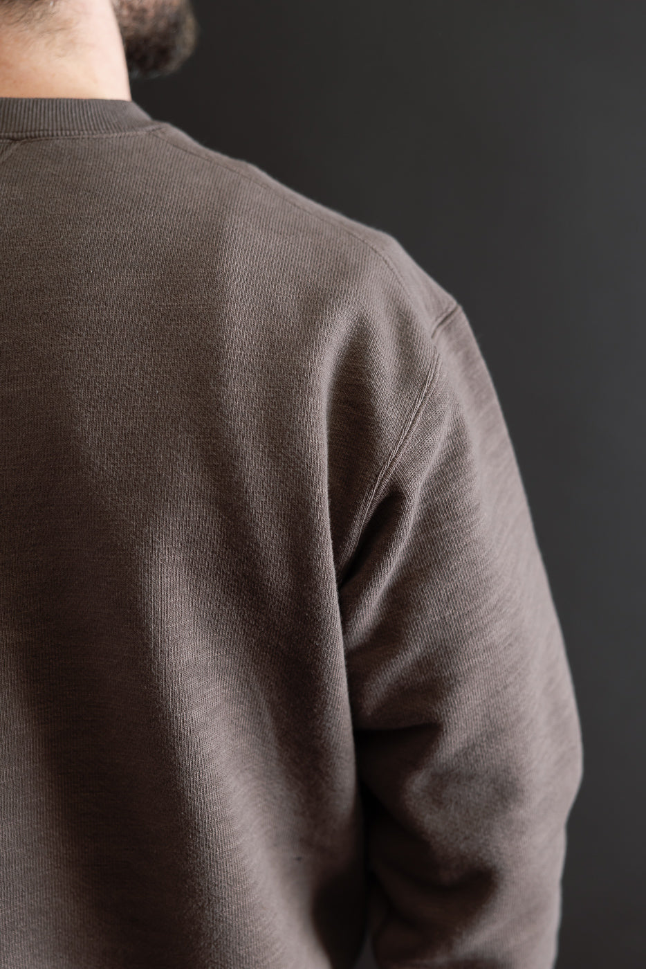 Close-up of the back and right side of a brown textured crewneck sweatshirt on a male model.