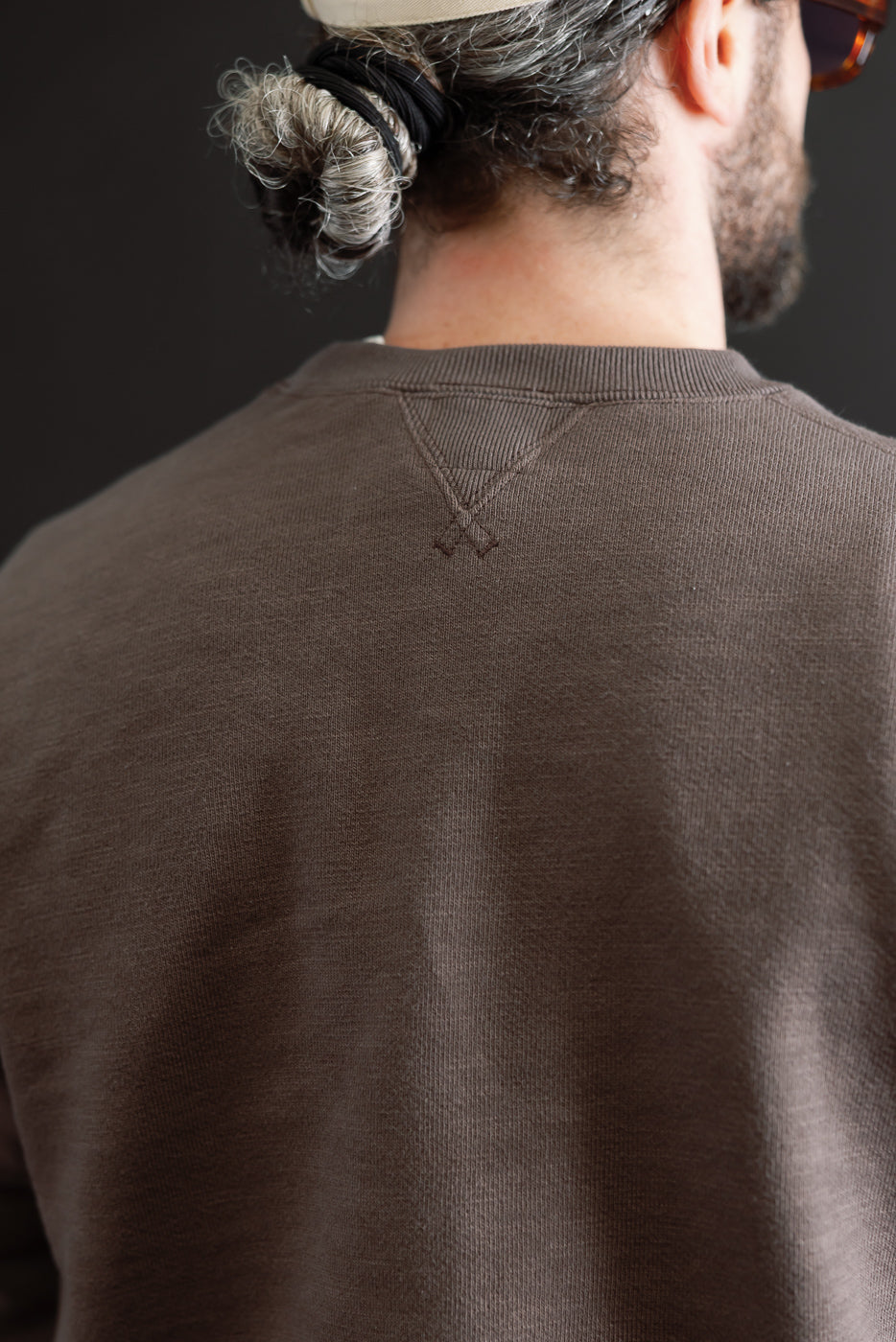 Close-up back view of a brown sweatshirt showing the ribbed neckline and V-stitch detail.
