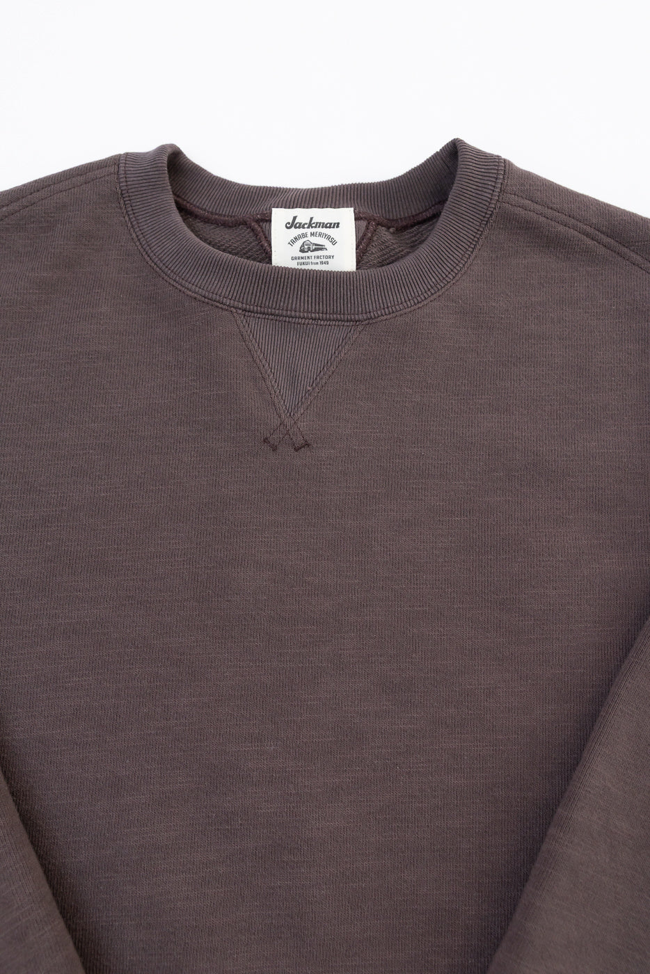 Close-up of the front neckline of a brown Jackman sweatshirt showing the tag and V-stitch.