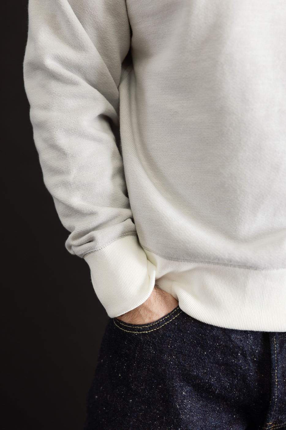 Close-up side view of a light grey sweatshirt hem and cuff on a 5'9