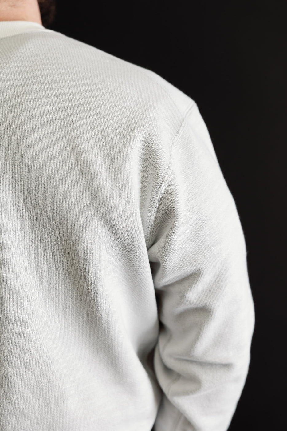 Close-up rear view of a light grey sweatshirt showing the back and shoulder fabric texture.